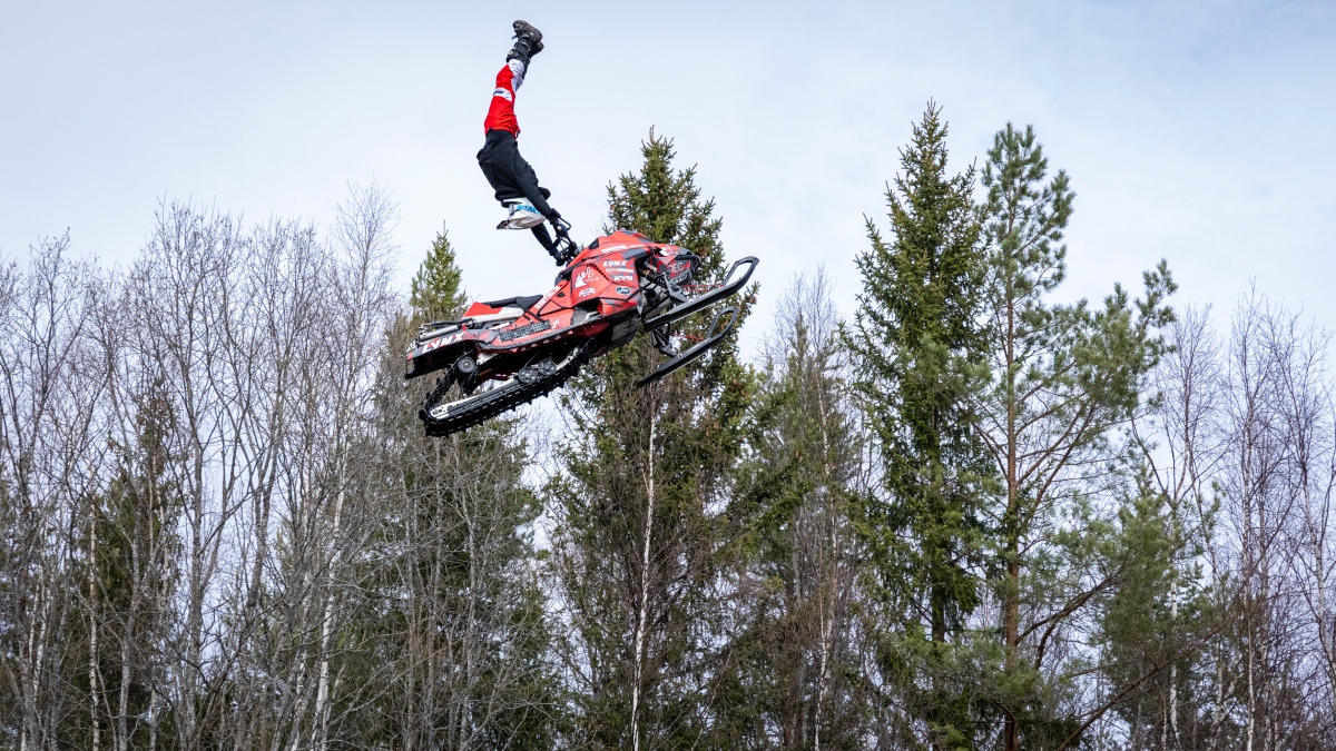Moottorikelkkailija tekee tempun ilmassa metsän yllä